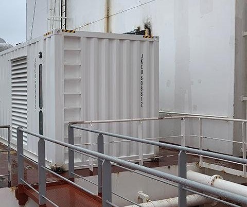 White containerised Cunmi generator set operating on the deck of a working vessel in port